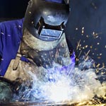 Worker dressed in protective uniform welding metal frame